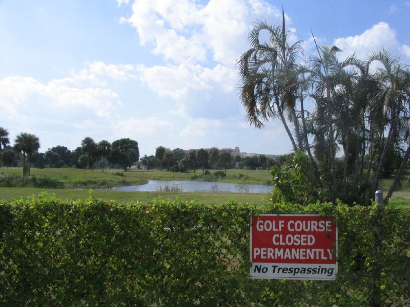 a golf course closed permanently with a no tressing sign in front of a green hedge