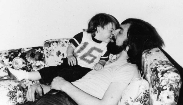 a man with beards kissing a baby sitting on a couch
