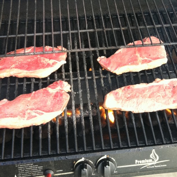 steaks on top of a grill with flame coming from the grill