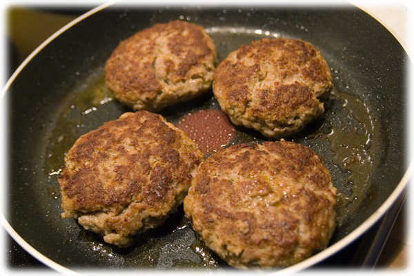 three cooked hamburger patties frying in a wok