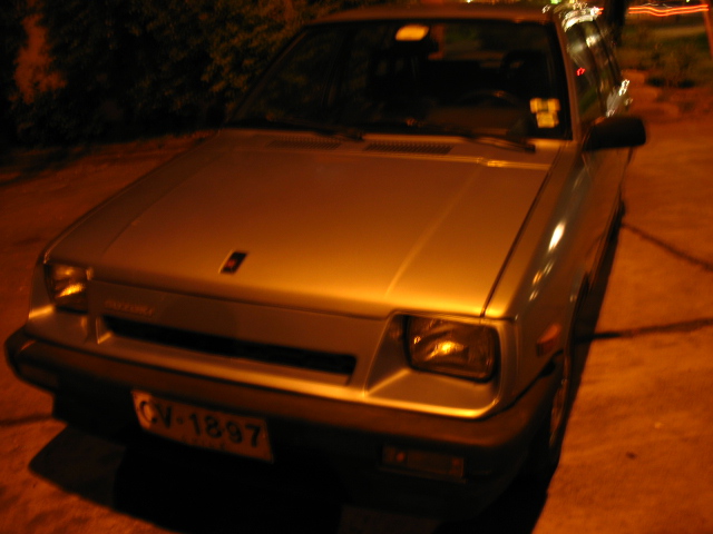 a silver, old, and rusty car sits in the dark