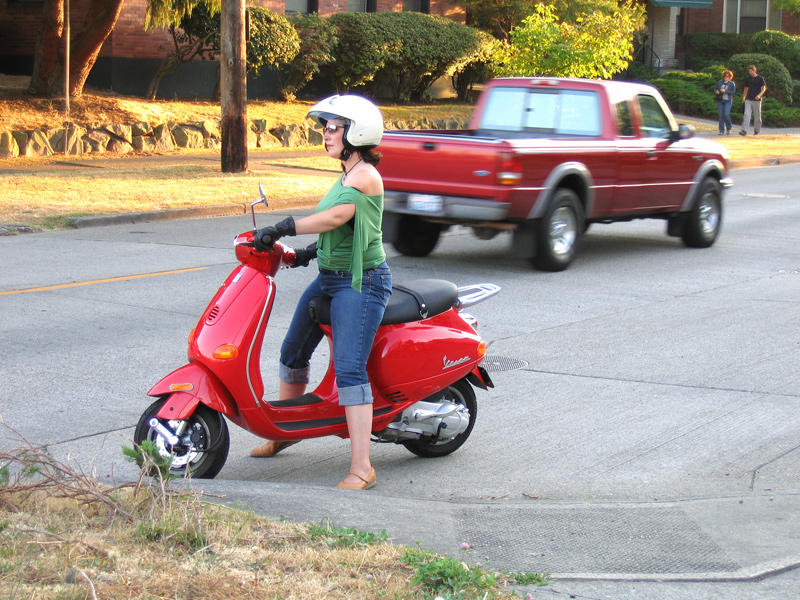 a woman in a helmet is riding a red scooter on the road