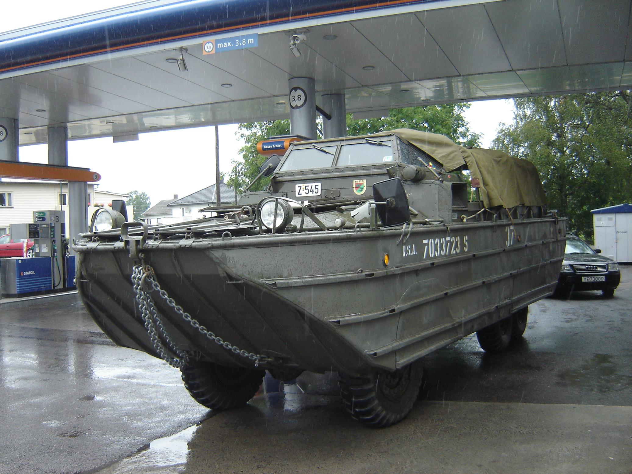 a boat with wheels is parked on the pavement near gas pumps