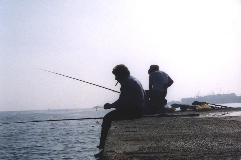 two people sitting on rocks and fishing by the sea
