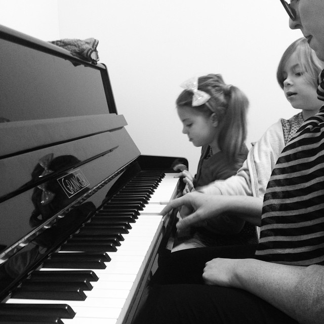 three people sit at a piano with one playing the keyboard