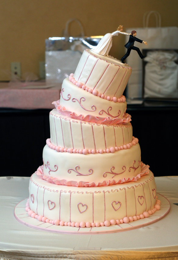 a wedding cake has pink decor and a figure on top