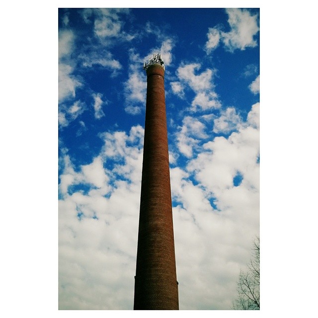 a tall chimney rises in the sky next to clouds