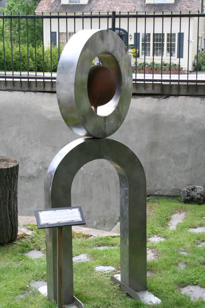 a metal sculpture on a lawn by a wall