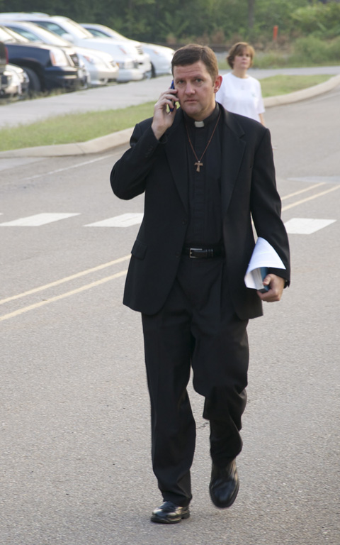 the young priest is walking down the street on his cell phone