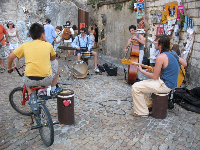 a musician playing music in the street as a man on a bicycle approaches