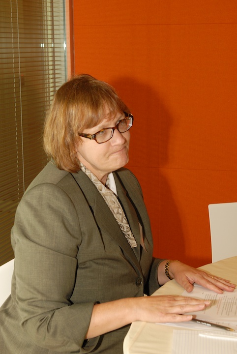 a woman in glasses sits at a desk and looks off
