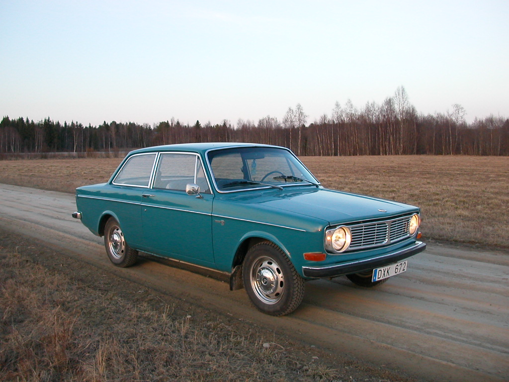 an old model blue station wagon parked on the side of a rural road