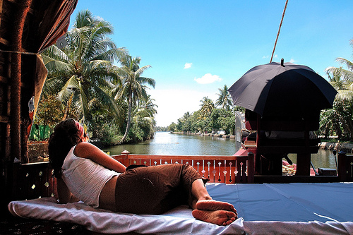 a woman sitting on a white towel by a body of water