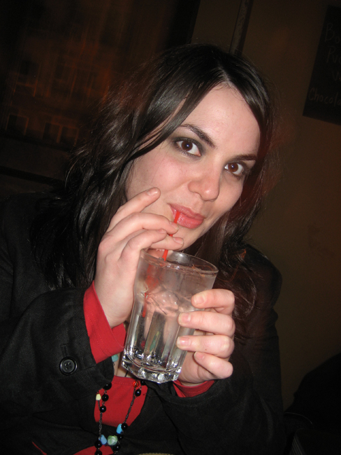 the woman is drinking from a glass while posing for the camera