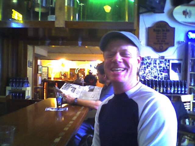 a man standing at a bar smiling and drinking wine