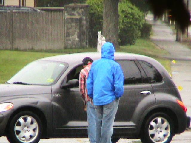 a boy in the rain with his surfboard on his hand standing in front of a car