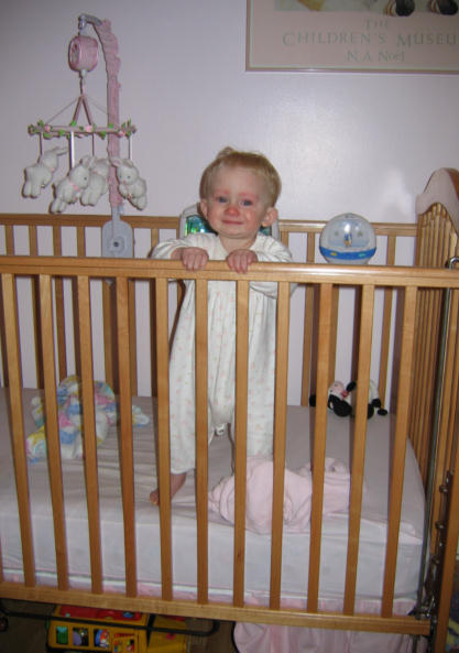 a baby in white clothes standing next to a ladder