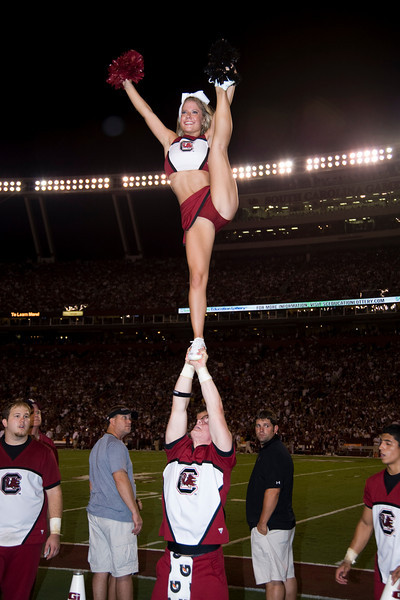 two cheerleaders stand on the sidelines while doing a balancing in front of an audience