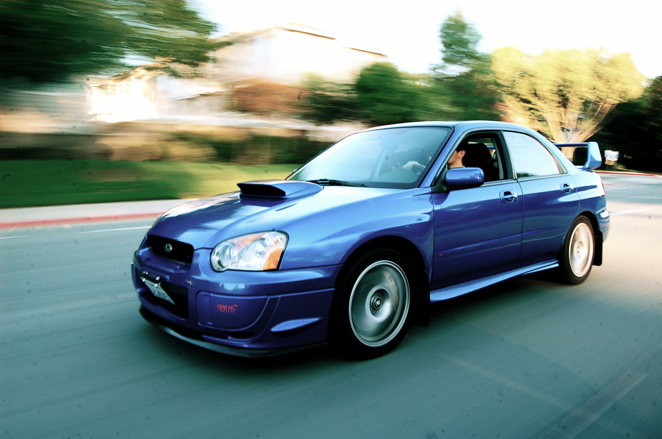 a blue car drives down a road near a parking lot