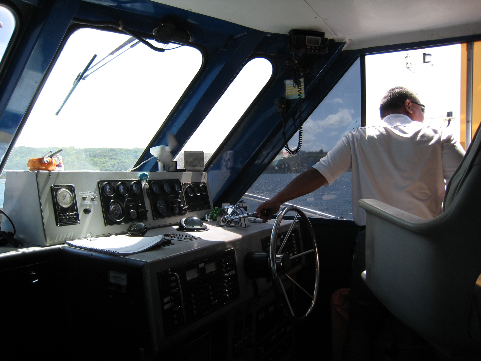 a man stands inside a boat's cockpit overlooking the water