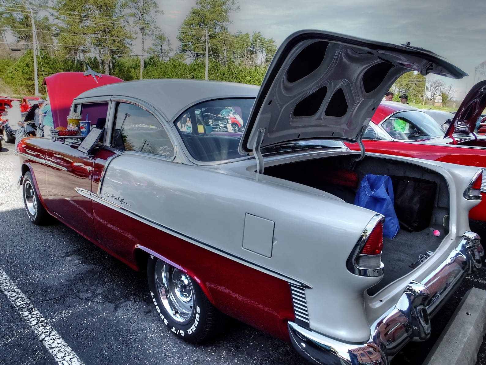 an older car with its trunk open, parked on the side of the road