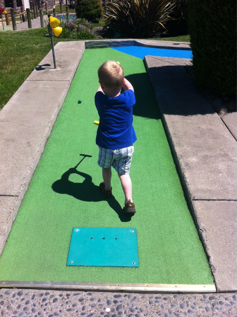 small child throwing a ball into the air on top of putting green