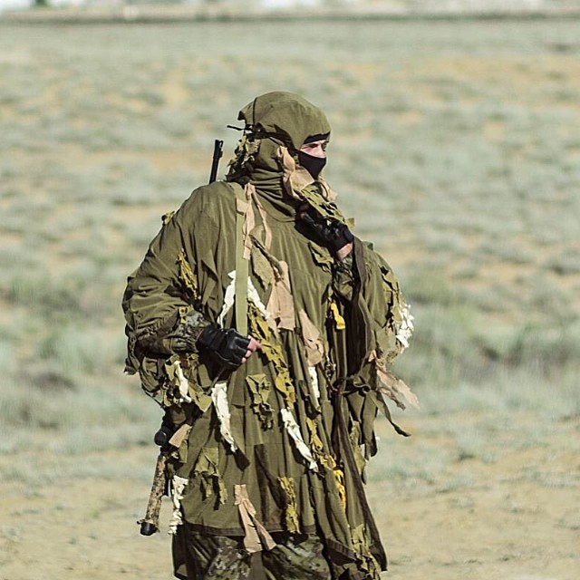 a man dressed in army clothes carrying a bag and walking on dirt