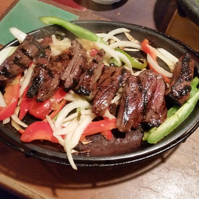 a steak dish with onions and peppers sitting on a plate