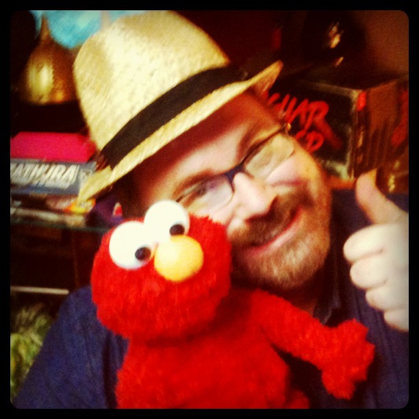 a man with a hat and eye glasses holds a large stuffed animal