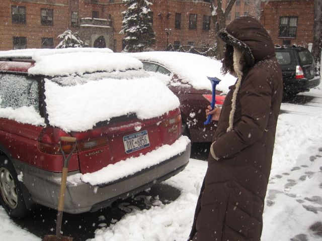 the man is using a shovel to clear the snow from his cars