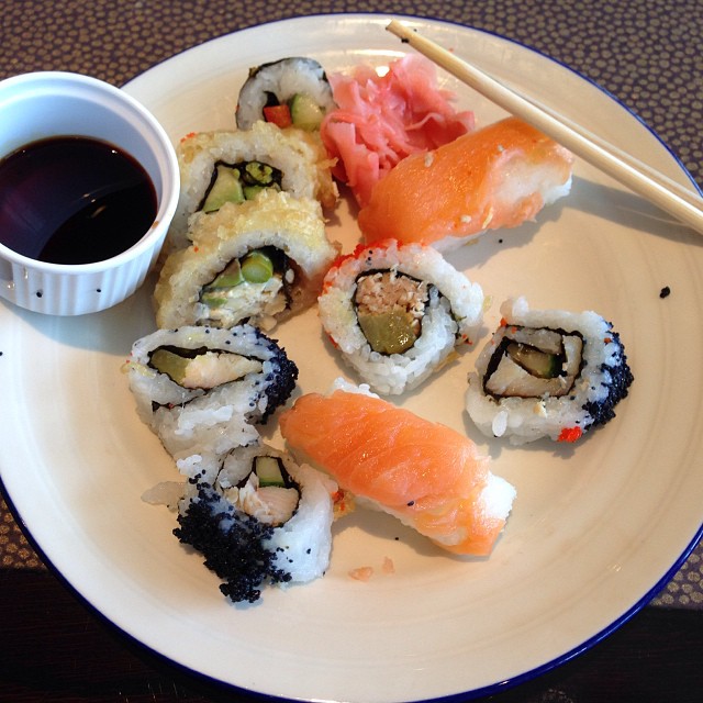 a white plate topped with sushi next to a cup of sauce