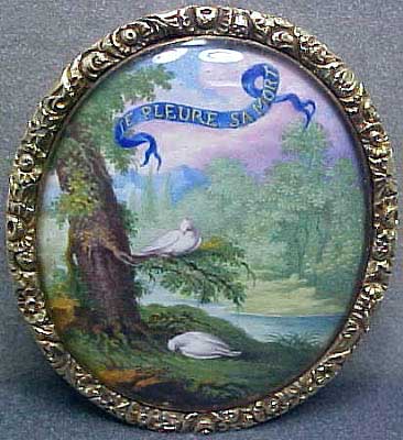 a small, antique broochle depicting birds sitting on the edge of a tree