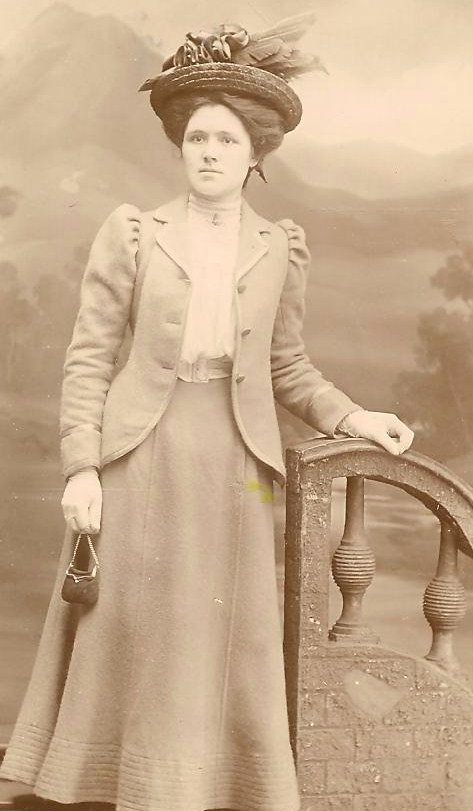 old time woman wearing long dress and hat standing