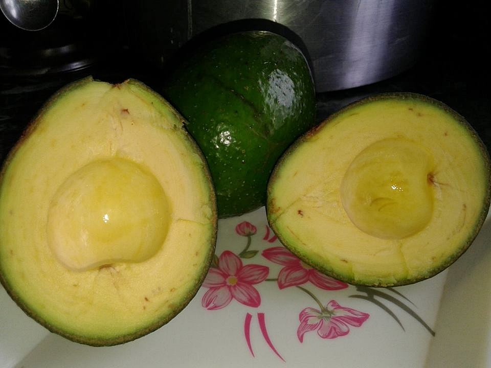 a small pile of avocado next to an open avocado on a tray