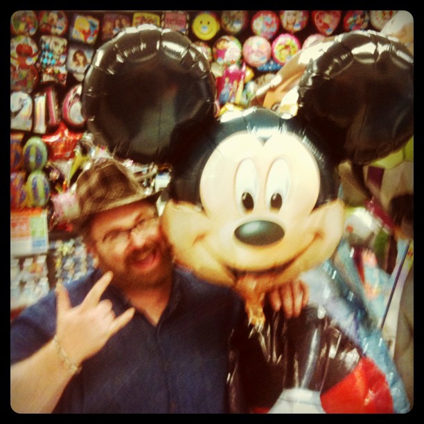 the man is smiling and posing for the camera with mickey mouse balloon