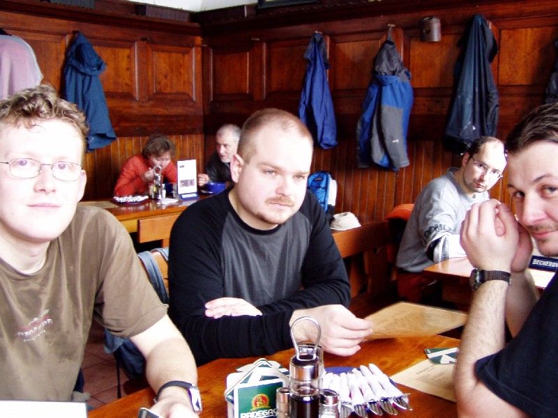 three men are sitting at a table and one has a cigarette