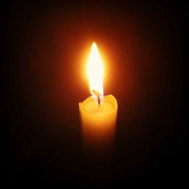 a candle lit up and on black with light coming from the top
