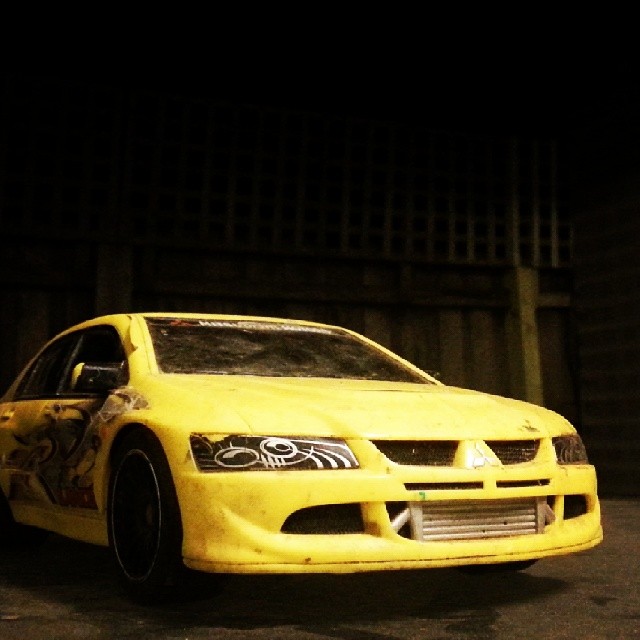 a yellow car with black rims parked by a fence