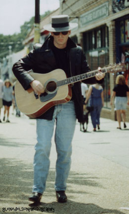 a man playing an acoustic guitar down a street