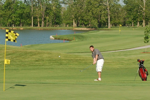 a man in grey shirt playing golf in front of a lake