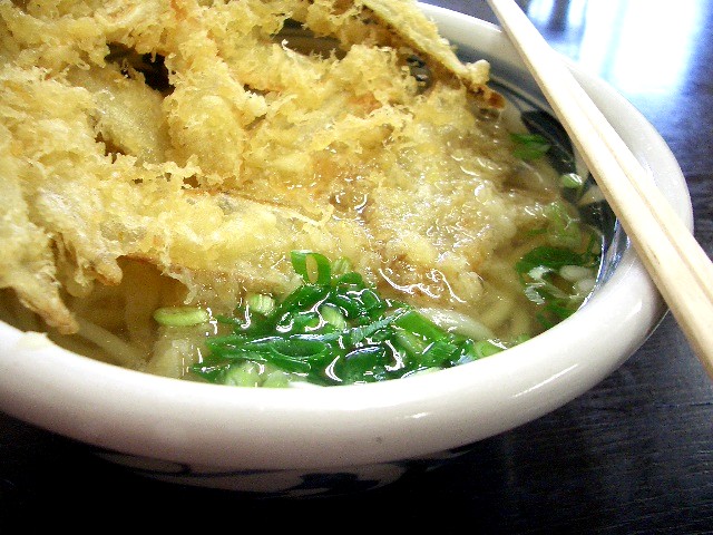 a bowl full of soup with green onions and chopsticks