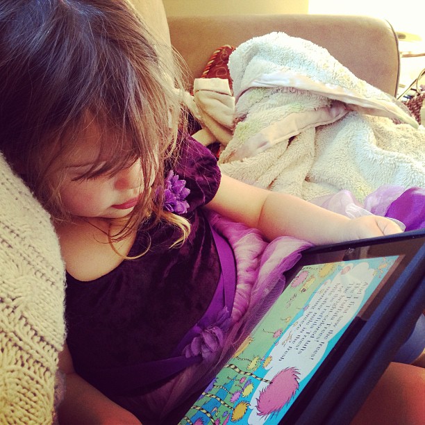 little girl laying on couch reading book wearing purple dress