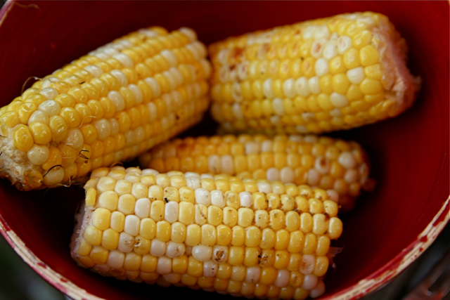 several corn cobs in a red bowl on top of a stove