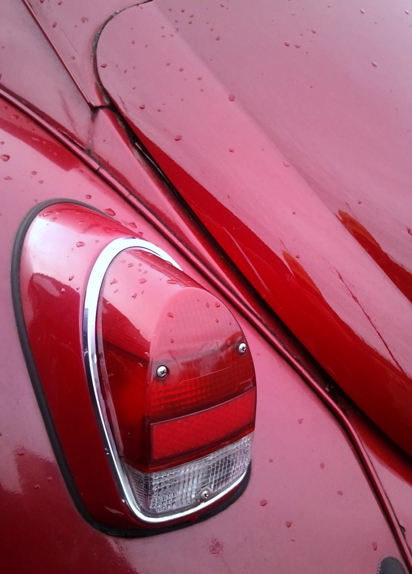a closeup of a shiny red car with rain drops