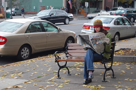 the woman sits on the bench in the city reading the paper