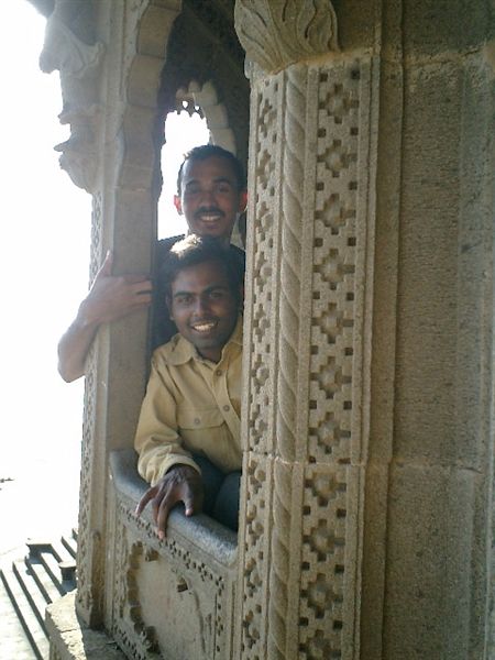 two men stand smiling in front of ornate stone pillars