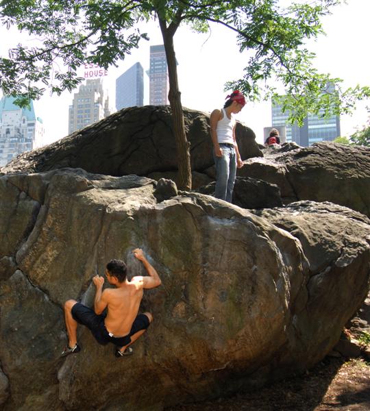 the man climbs on a large boulder in front of a couple of other people