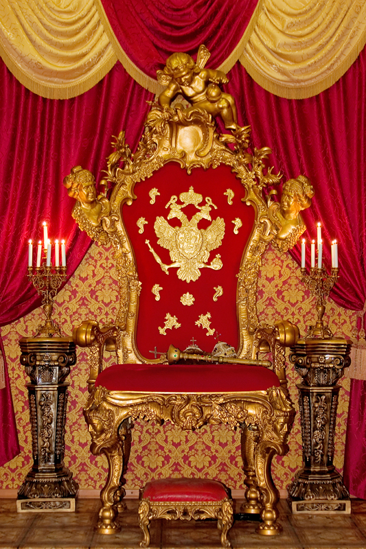 a fancy gold throne with red walls and chairs