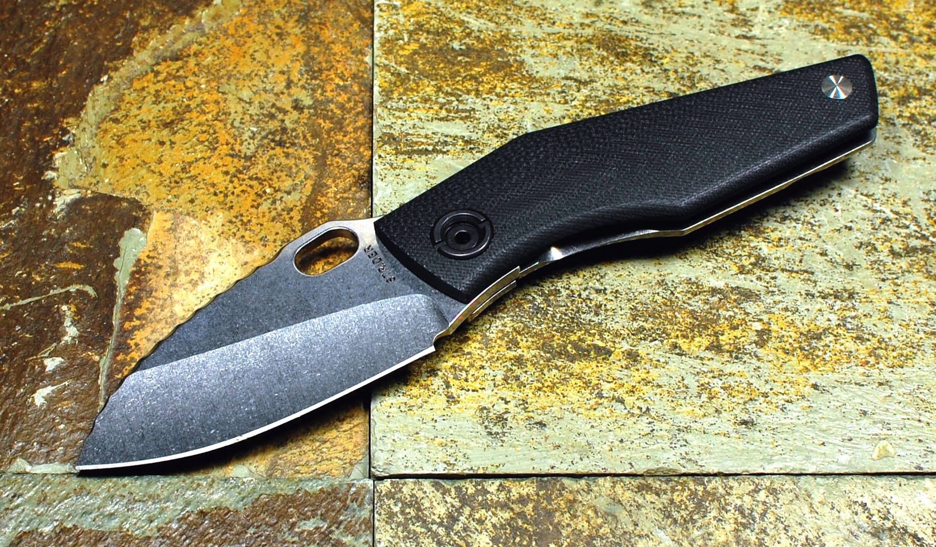 black folding knife resting on a stone surface