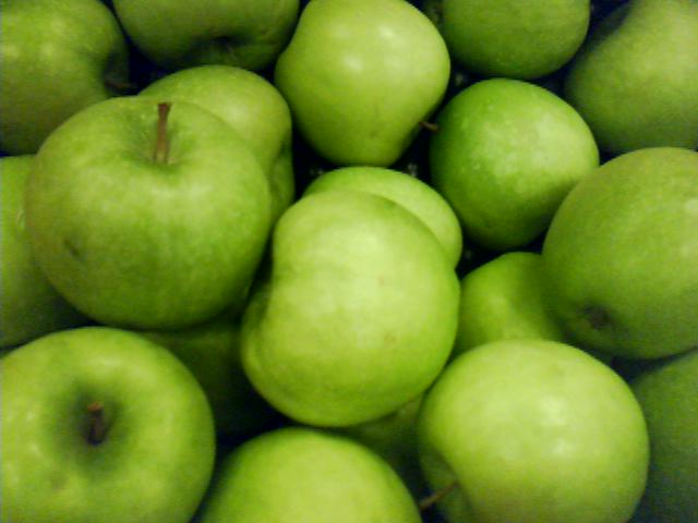 a pile of green apples are sitting in a glass bowl
